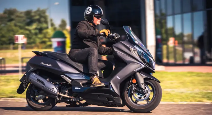 Mężczyzna w kasku jedzie na skuterze Kymco Downtown 125. Poznaj kymco downtown 125 dane techniczne.