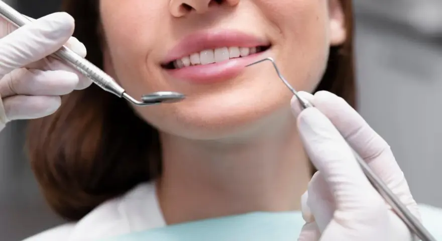 Uśmiechnięta kobieta podczas zabiegu remineralizacji szkliwa. Dentysta używa lusterka i sondy.