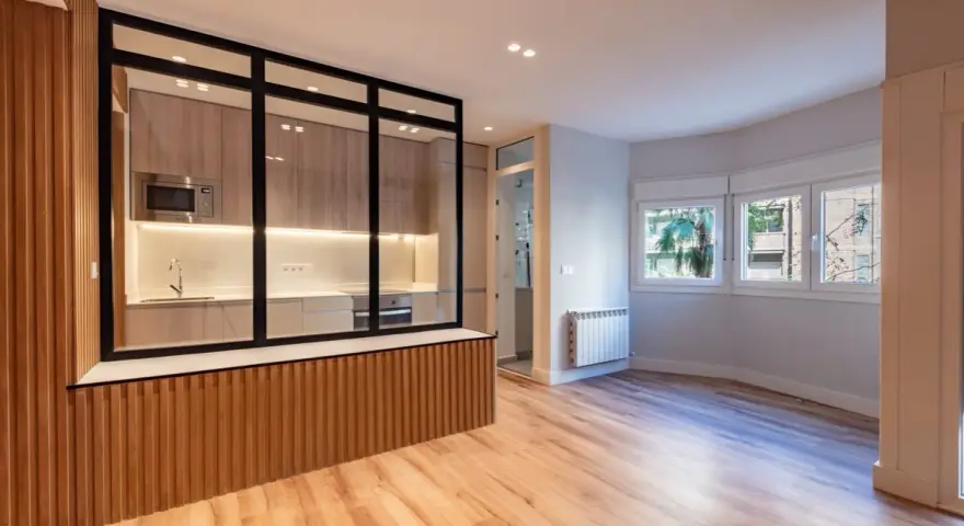 Entrada salón recibidor integrado. Cocina moderna con cristalera y madera, conectada a un luminoso salón con ventanas.