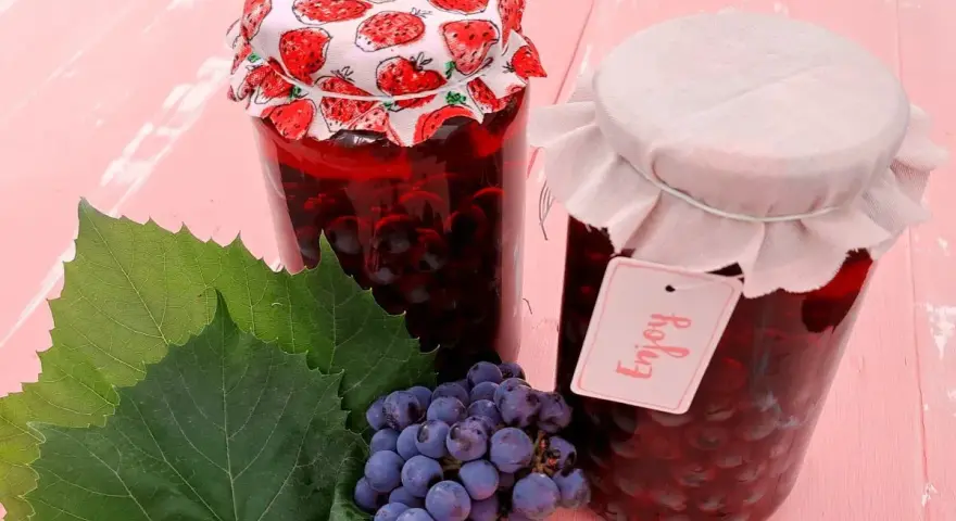 Słoiki z przetworami z winogron, przypominającymi wino z mrożonych winogron. Obok kiść winogron i liście.