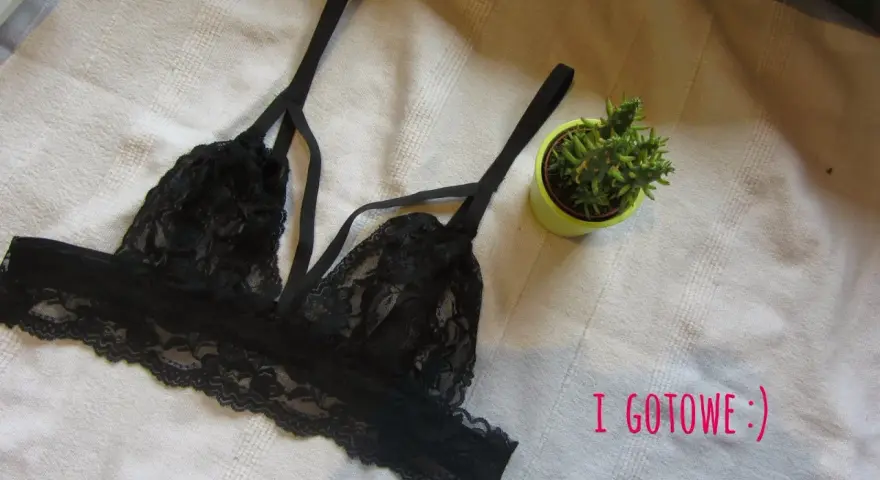 Czarny, koronkowy biustonosz typu bralette, idealny do obszywania bielizny. Obok mała roślinka w doniczce.