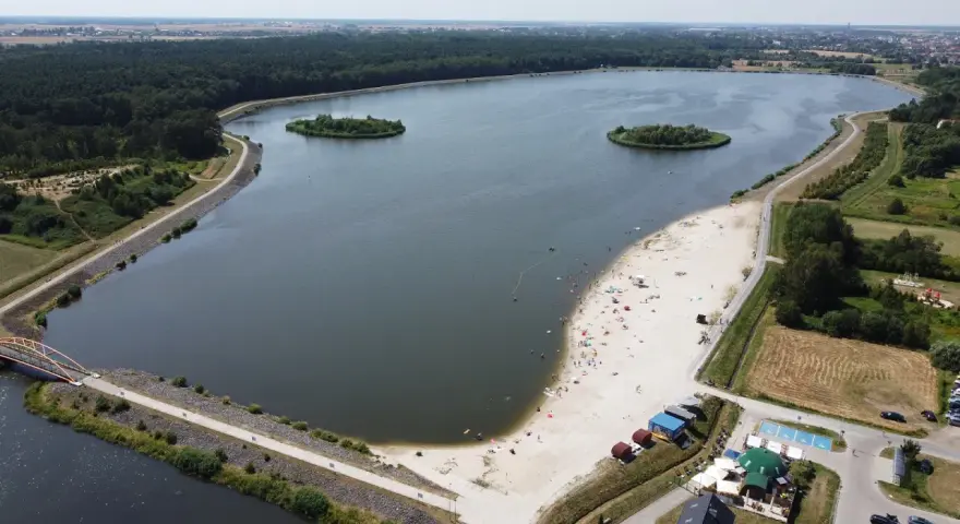Opolskie atrakcje: piaszczysta plaża nad jeziorem, wyspy, las i mostek. Ludzie odpoczywają i kąpią się.