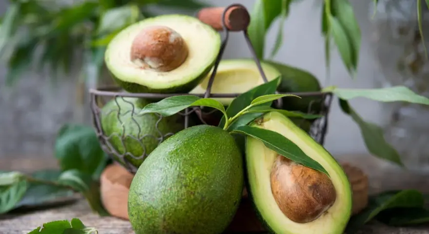 Des avocats frais, entiers et coupés en deux, dans un panier. Pour savoir comment avoir un avocatier qui donne des fruits, il faut de la patience et de bons soins.