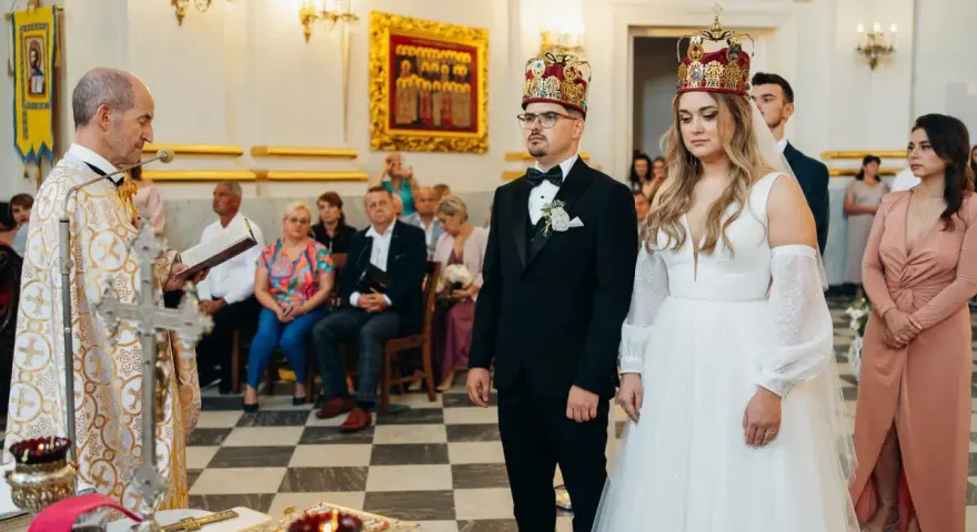 Uroczystość zaślubin w cerkwi. Pan młody, niczym ludowy grajek z Ukrainy, w eleganckim czarnym garniturze, z narzeczoną w białej sukni, przyjmują błogosławieństwo.