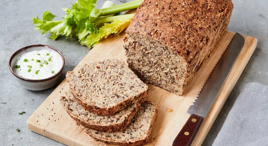 Ein rustikales Chia Brot, frisch aufgeschnitten, mit Sellerie und Dip auf einem Holzbrett.