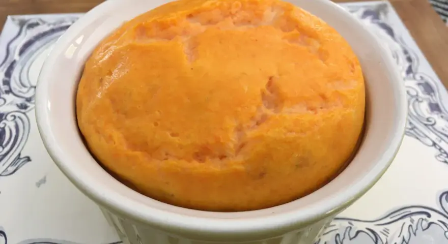 Un délicieux flan de carottes, doré et moelleux, servi dans un ramequin blanc sur une assiette décorée.