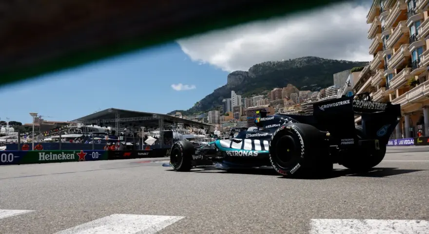 Coche de clasificación F1 en Mónaco, con el mar y edificios de lujo de fondo.
