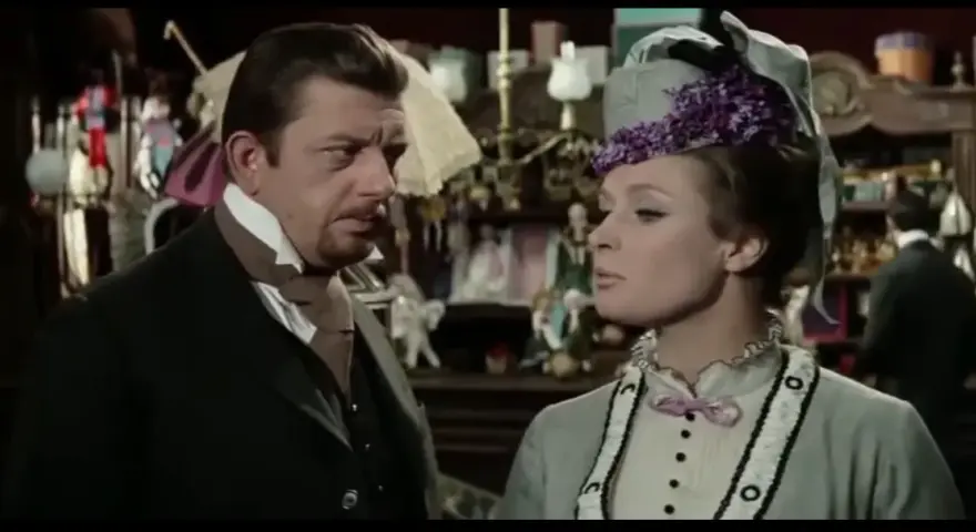 Mariusz Dmochowski w filmach, u boku pięknej kobiety w kapeluszu, w sklepie pełnym lalek i bibelotów.