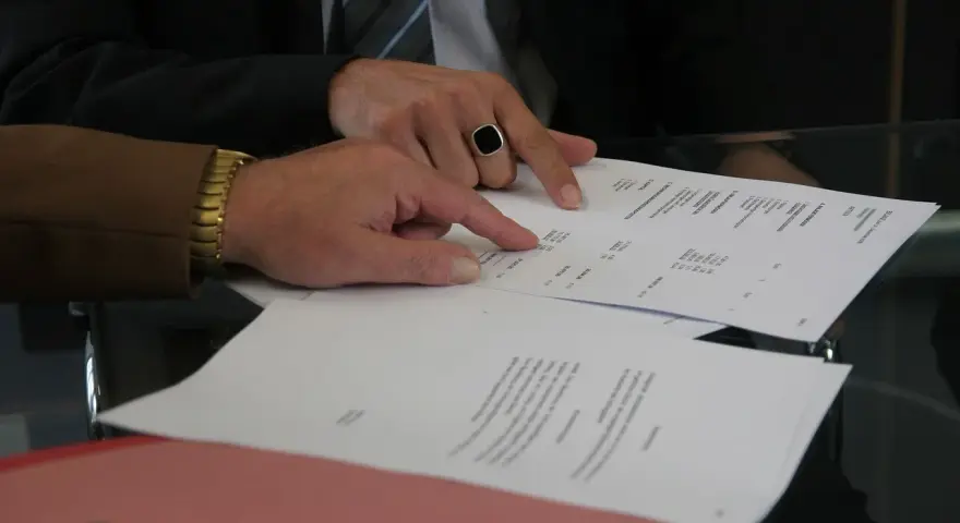 Dwóch mężczyzn analizuje dokumenty. Jeden z nich, w garniturze i z pierścieniem na palcu, wskazuje na tabelę. Pytanie: Millennium Bank zajęcie egzekucyjne jak sprawdzić?