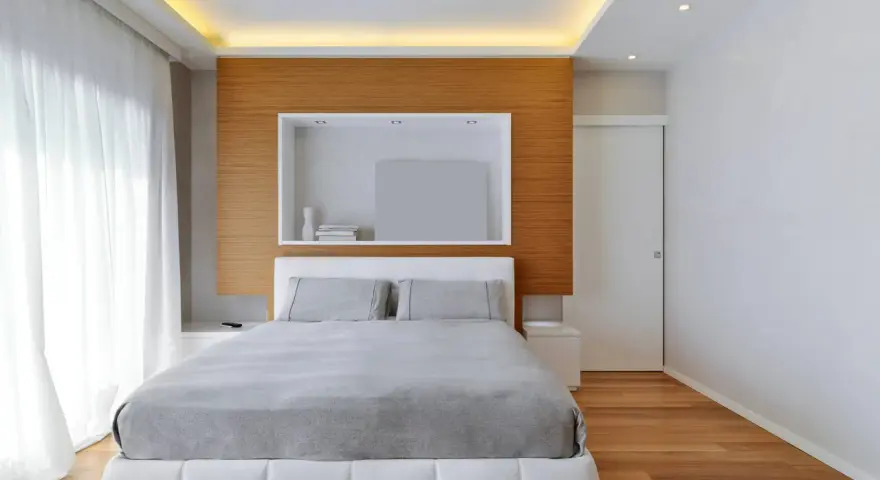 Camera da letto con letto bianco, lenzuola grigie e un moderno controsoffitto con illuminazione a LED.