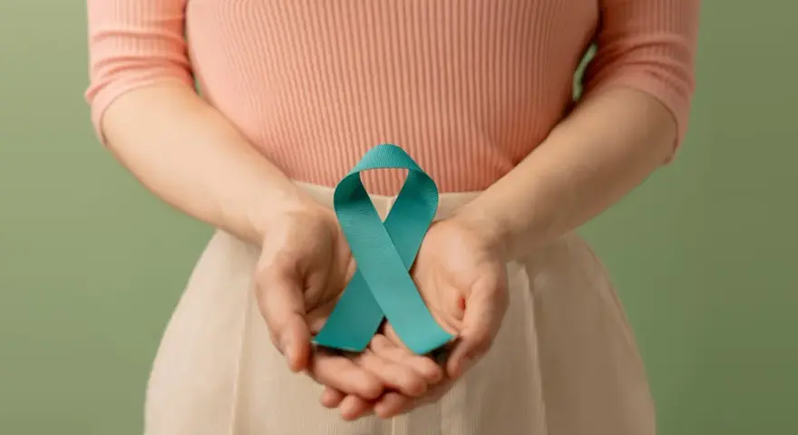 Dłonie trzymają turkusową wstążkę, symbolizującą wsparcie dla kobiet z PCOS. Dowiedz się, pcos co to.