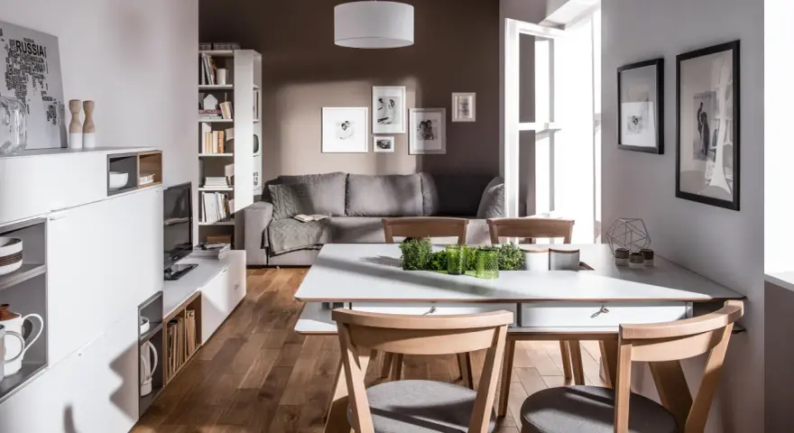 Nowoczesny salon z szarą kanapą i drewnianymi krzesłami. Czy brązowy pasuje do szarego? Tak, w tej aranżacji tworzy przytulną atmosferę.