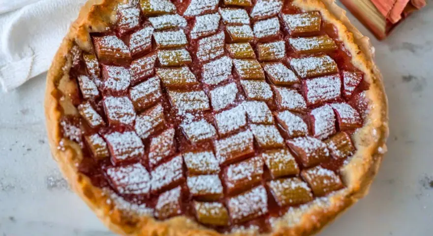 Tarta z rabarbarem posypana cukrem pudrem, obok łodygi rabarbaru.