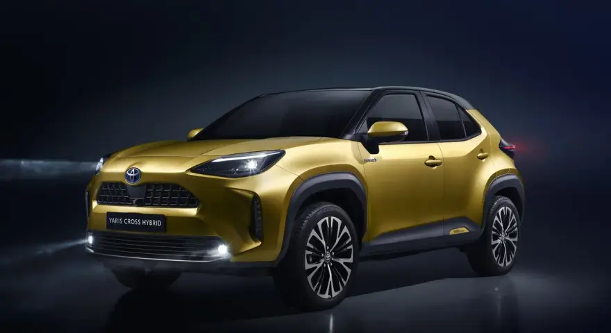 Złoty Toyota Yaris Cross Hybrid z włączonymi światłami na ciemnym tle.