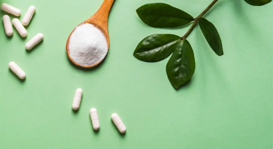 Vita C-vitaminer i kapslar och pulver på en sked, med gröna blad.