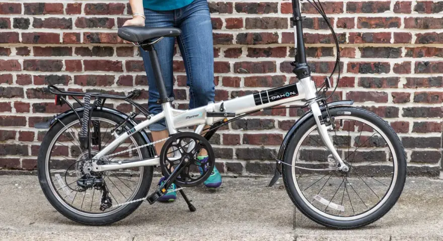 A person stands next to a silver Dahon Mariner folding commuting bike, ready for their next urban adventure.