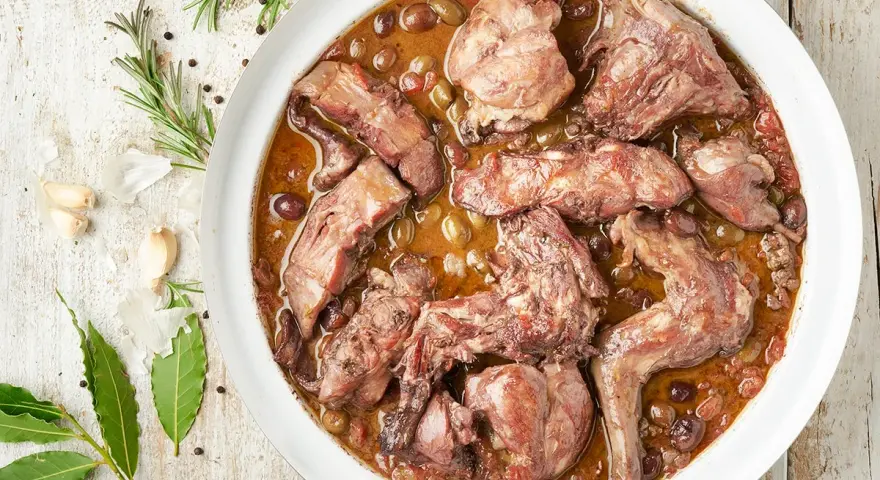 Coniglio in padella, un piatto succulento con olive e aromi, pronto per essere gustato.