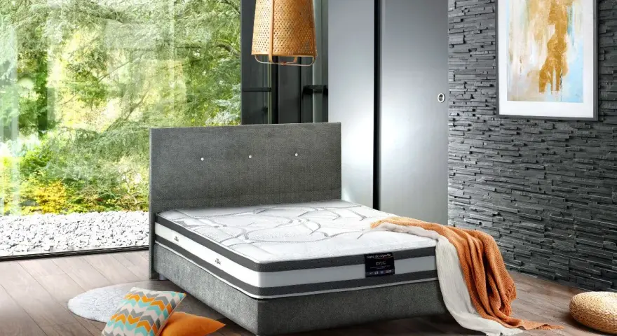 Un lit moderne avec un matelas de dimension queen size, des coussins colorés et une couverture orange sur un parquet en bois.