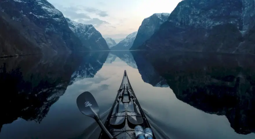 Kajakpaddling i en norsk fjord med snöklädda berg som speglar sig i det lugna vattnet. En fantastisk utsikt över son Norge.
