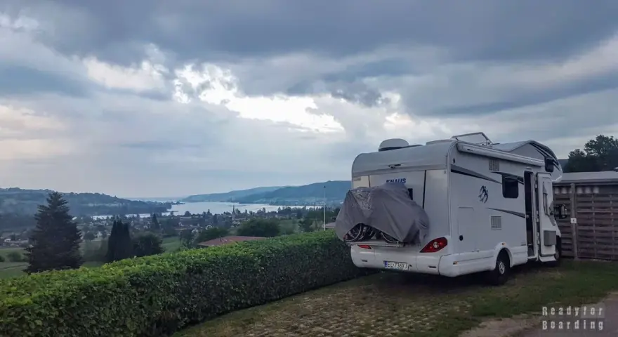 Kamper zaparkowany na kempingu w Czeskiej Szwajcarii, z widokiem na jezioro i wzgórza.