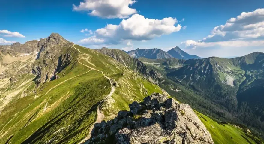 Widok na szlak prowadzący na Kasprowy Wierch. Zielone zbocza górskie, skaliste szczyty i błękitne niebo z chmurami.