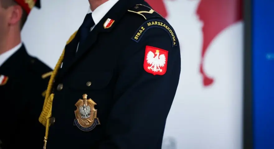 Urzędnik w granatowym mundurze z godłem Polski i napisem "STRAŻ MARSZAŁKOWSKA" na rękawie.