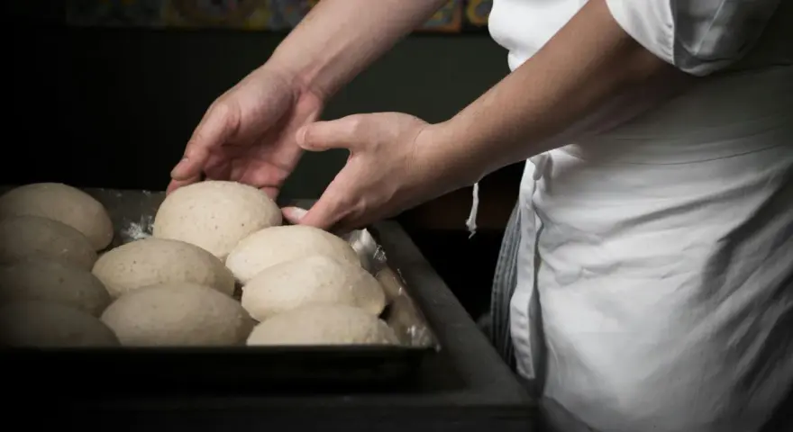 Mani esperte sistemano impasti per pizza, un mestiere che fa riflettere su quanto guadagna un pizzaiolo al mese.