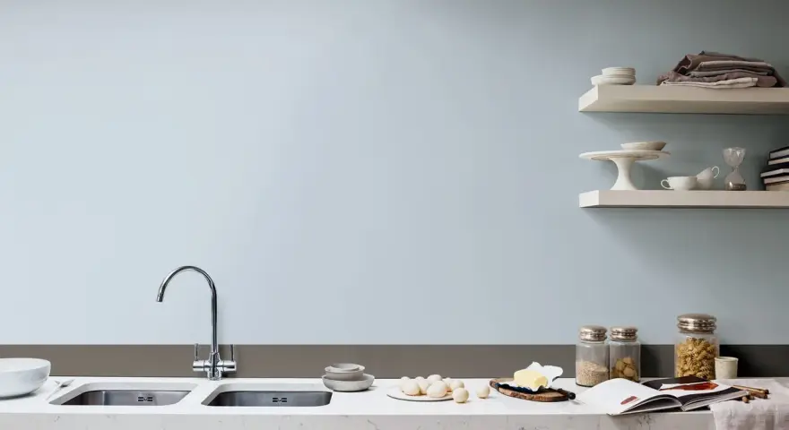 Jasne, pastelowe kolory ścian w kuchni tworzą spokojną atmosferę. Na blacie widać jajka, masło i otwartą książkę kucharską.