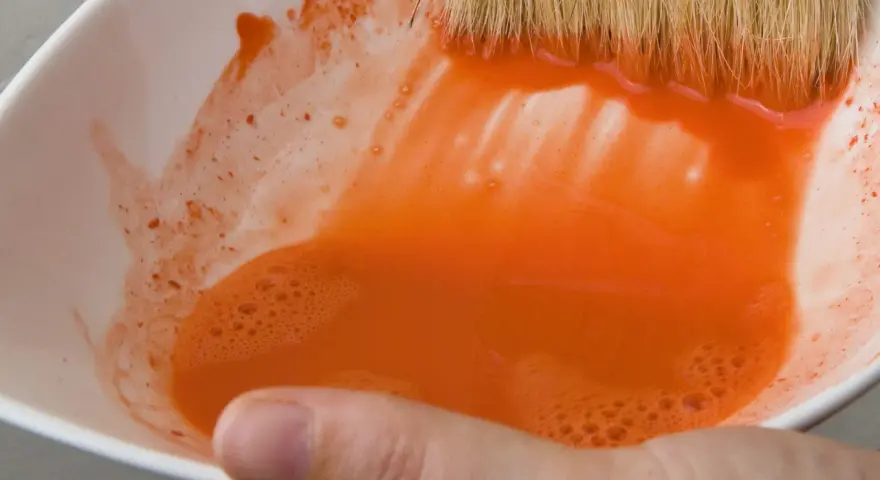 Maintenant, où jeter l'eau de rinçage des pinceaux ? Une main tient un bol blanc rempli d'eau orange trouble.