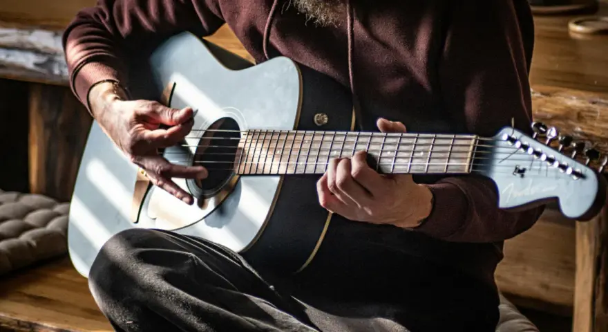 Mann spielt Akustikgitarre, Hände auf Saiten und Plektrum.