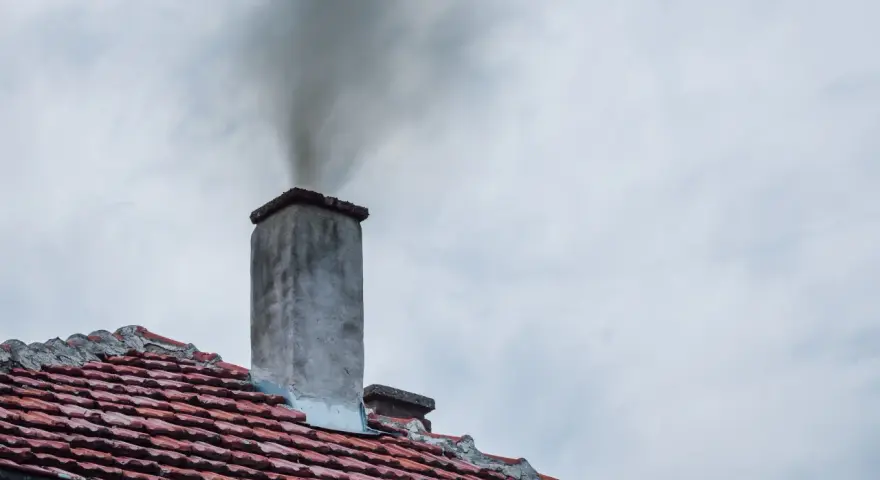 Dym wydobywający się z komina na tle pochmurnego nieba.