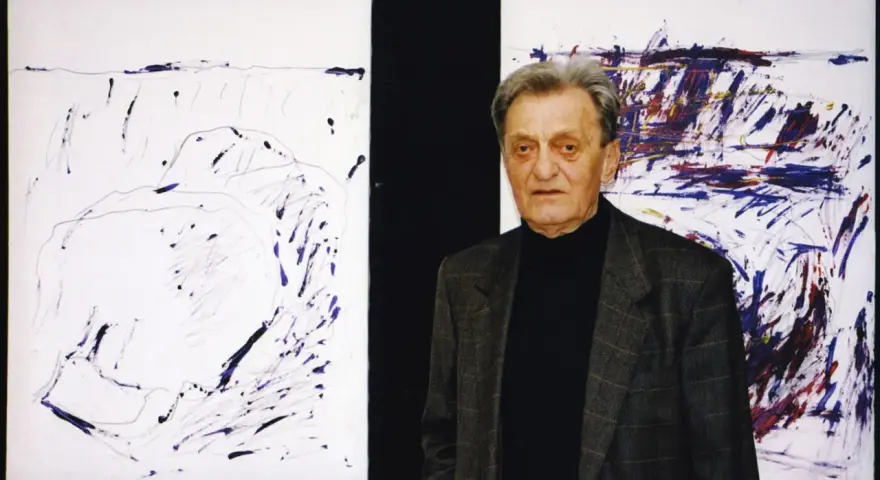 Jacek Sempoliński, artysta, stoi obok swoich abstrakcyjnych obrazów.