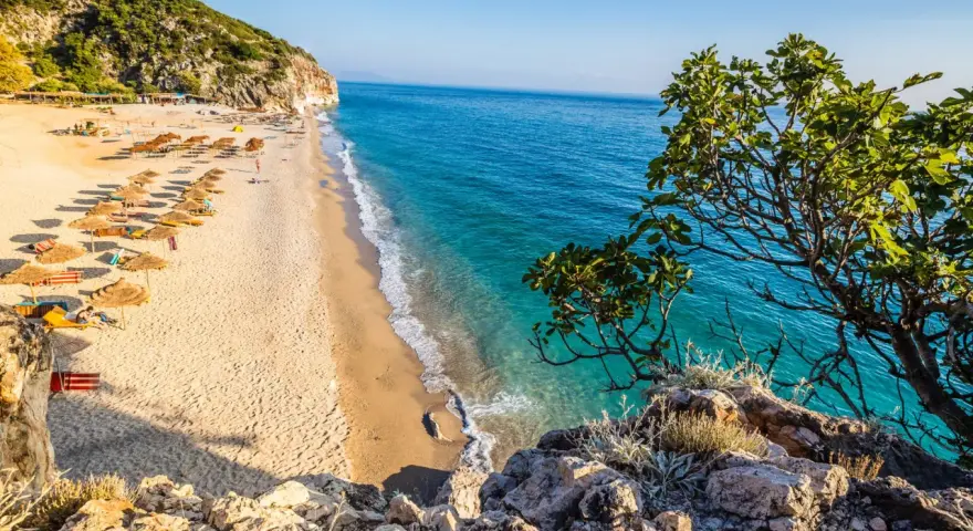 Piękna plaża w Albanii, gdzie ceny są przystępne. Słoneczny dzień, turkusowa woda i zielone wzgórza.