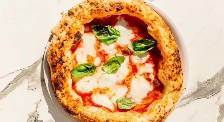 Eine echte italienische Pizza Margherita mit geschmolzenem Mozzarella, Tomatensauce und frischem Basilikum auf einem Marmortisch.