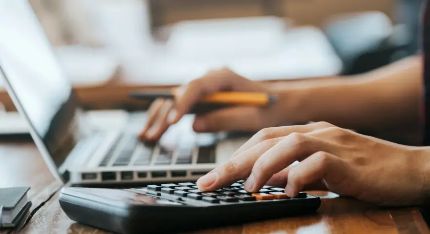 Hände bedienen Laptop und Taschenrechner. So lässt sich die Kaution in Raten zahlen und die Finanzen im Blick behalten.