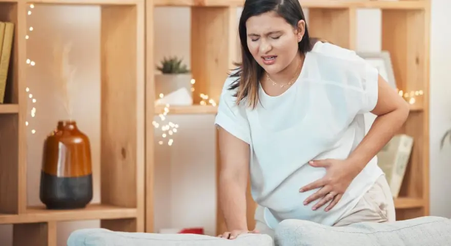Frau mit schmerzverzerrtem Gesicht hält ihren Bauch, als ob sie Wehen erkennen würde.