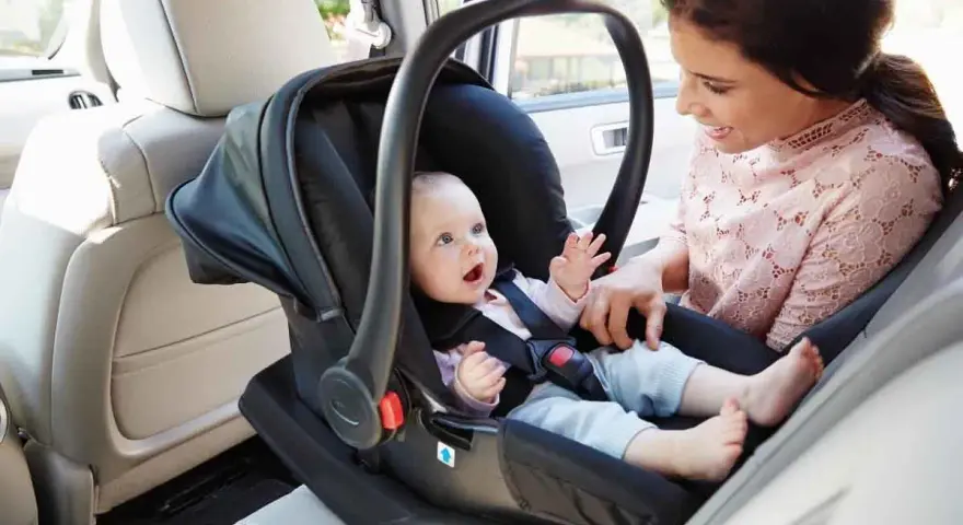 Uśmiechnięta mama patrzy na swojego **noworodka w foteliku samochodowym**, gotowego na podróż.