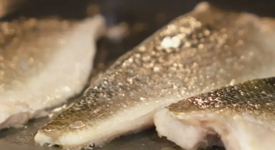 Filetes de lubina a la donostiarra dorándose en una sartén.