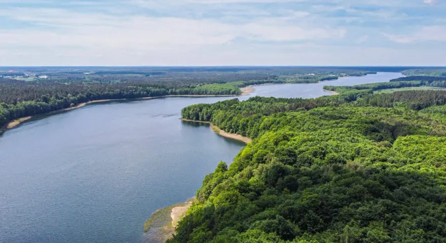Malownicze jezioro otoczone lasem, idealne miejsce na nietypowe atrakcje Mazury. Widok z lotu ptaka na spokojną taflę wody i bujną zieleń.
