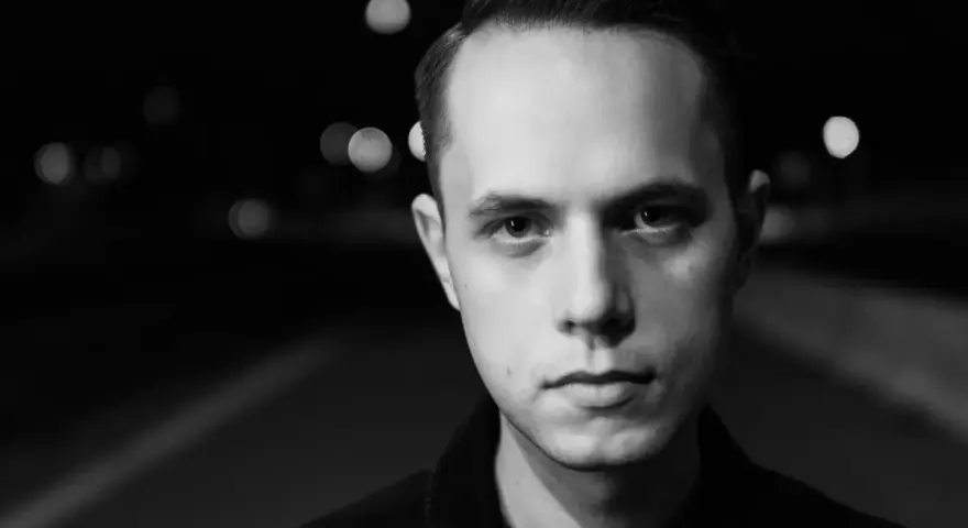 Młody mężczyzna, Gibbs producent, patrzy wprost w obiektyw na tle nocnych świateł.