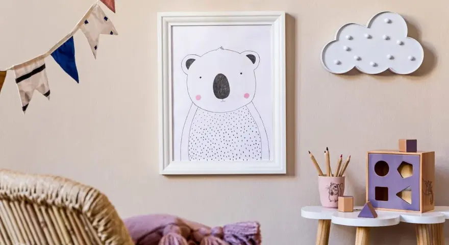 Adorable cuadros infantiles de un koala y una nube decoran la pared de una habitación. Una guirnalda de banderines alegra el ambiente.