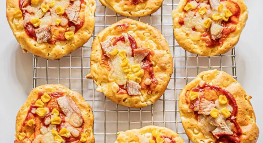 Mini pizze z serka wiejskiego, z kukurydzą i kawałkami mięsa, na metalowej kratce.