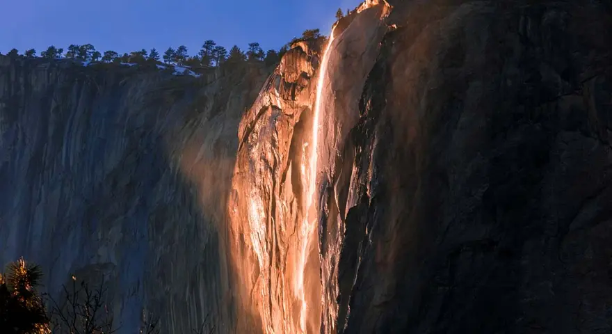 La luz del atardecer ilumina una cascada de fuego en un acantilado rocoso, creando un espectáculo natural.