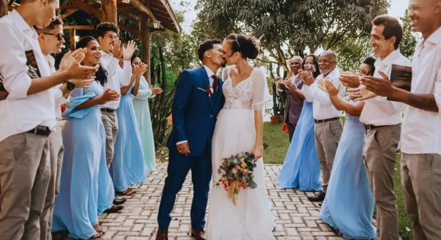 Un couple s'embrasse lors d'un mariage intime, entouré d'invités applaudissant.