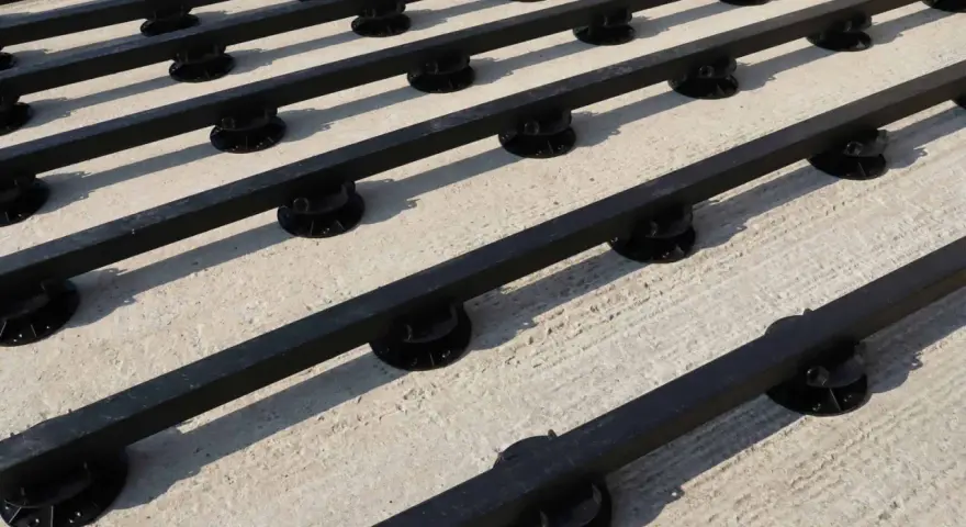Rows of black synthetic lumber are elevated on black adjustable pedestals, creating a modern deck base on a concrete surface.
