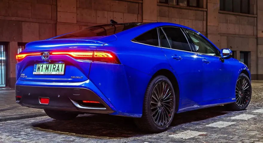 Niebieska Toyota Mirai z podświetlonymi światłami tylnymi stoi na brukowanej ulicy nocą.