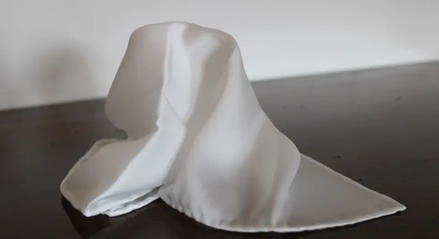 Un fazzoletto bianco di seta, drappeggiato su un tavolo scuro. Il suo significato è legato alla purezza e all'eleganza.