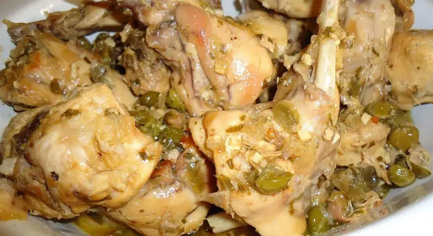Piatto fumante di coniglio alla cacciatora in bianco, con olive verdi e erbe aromatiche. Un classico della cucina italiana.