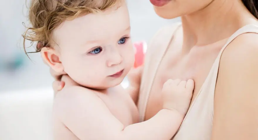 Ein Baby mit blauen Augen und zerzaustem Haar wird von seiner Mutter gehalten. Es ist fast 46 Wochen alt und durchläuft einen Entwicklungsschub.