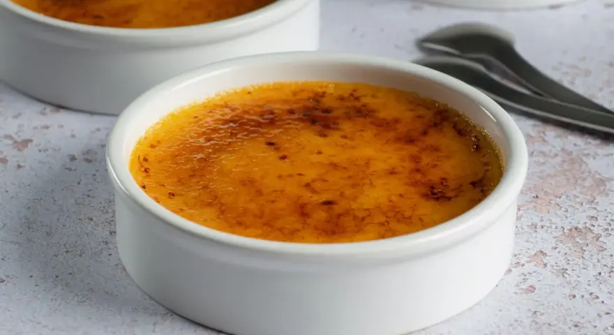 Dwa kremowe desery w białych naczyniach, z chrupiącą, karmelizowaną skórką. Crème brûlée czy crema catalana? Wybór należy do Ciebie!